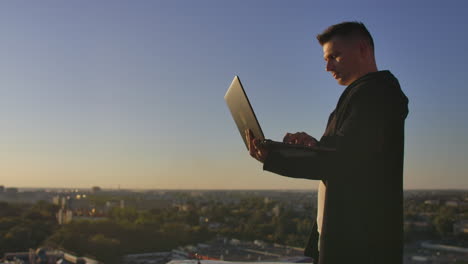 Programmer-a-hacker-is-on-the-roof-with-a-laptop-at-sunset-says-error-code-on-the-keyboard-and-looking-at-the-city-view.